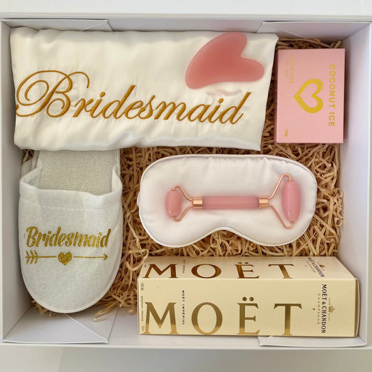 Satin dressing gown with gold stitching reading "bridesmaid", White slippers with gold font reading ""bridesmaid" , white satin eye mask, mini moet bottle, Coconut ice candy, Quartz face roller massager with Rose Quartz Gua Sha.  all packaged in a beautiful magnetic box with ribbons and personalized message, Gratefully gifted Christchurch  new zealand 